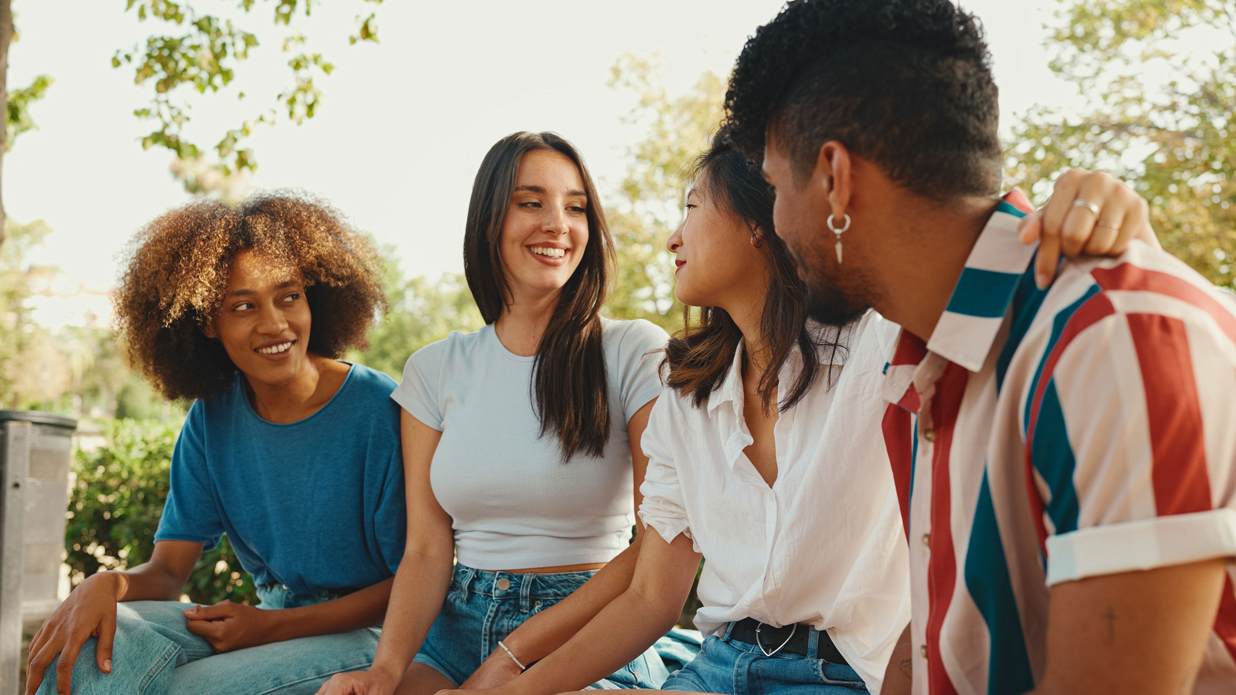 four people smiling and talking to each other on a bench outside